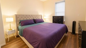 A bedroom with a bed, bedside tables, a dresser, and a window. - Soulard King 1BR w Washer & 370 Mbps Wi-Fi (St. Louis)