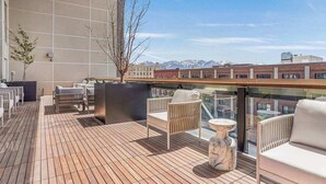 A rooftop terrace with wooden flooring, white sofas, and a marble table.
