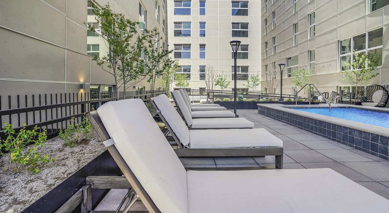 A rooftop pool area with lounge chairs, a swimming pool, and a building in the background.