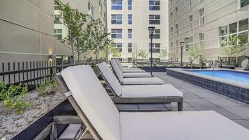 A rooftop pool area with lounge chairs, a swimming pool, and a building in the background.