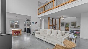 Un vaste espace de vie doté d’un haut plafond, d’un canapé blanc, d’une table à manger avec des chaises rouges et d’un balcon avec des balustrades en bois.