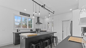 Une cuisine moderne dotée d’un îlot central, de tabourets de bar, d’une grande fenêtre et d’une enseigne indiquant « PRODUITS FRAIS ».