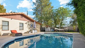Una piscina con bordo piastrellato, una sedia a sdraio e un'amaca.