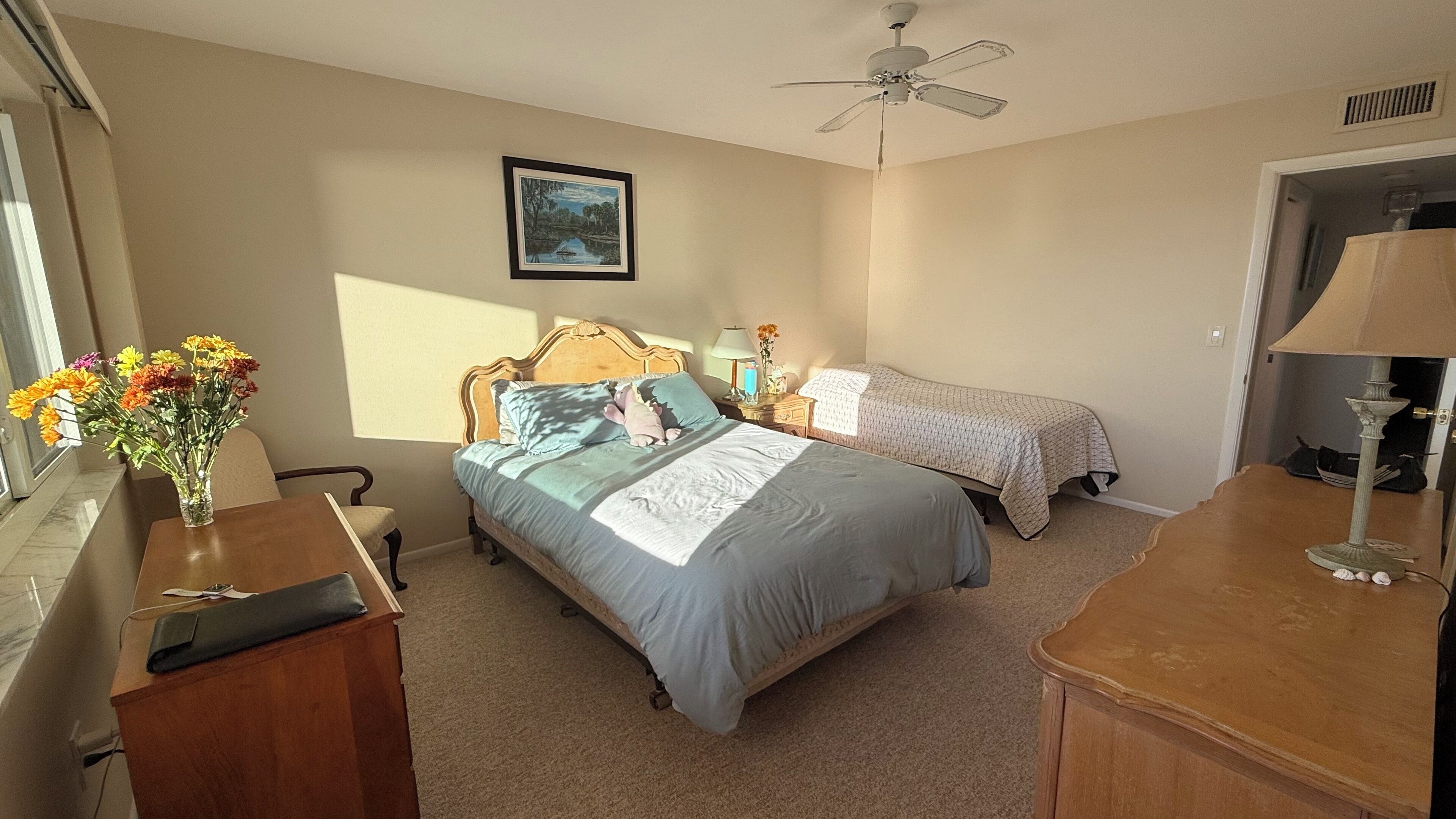 A bedroom with a bed, a nightstand, a lamp, a ceiling fan, and a window with a view of trees.