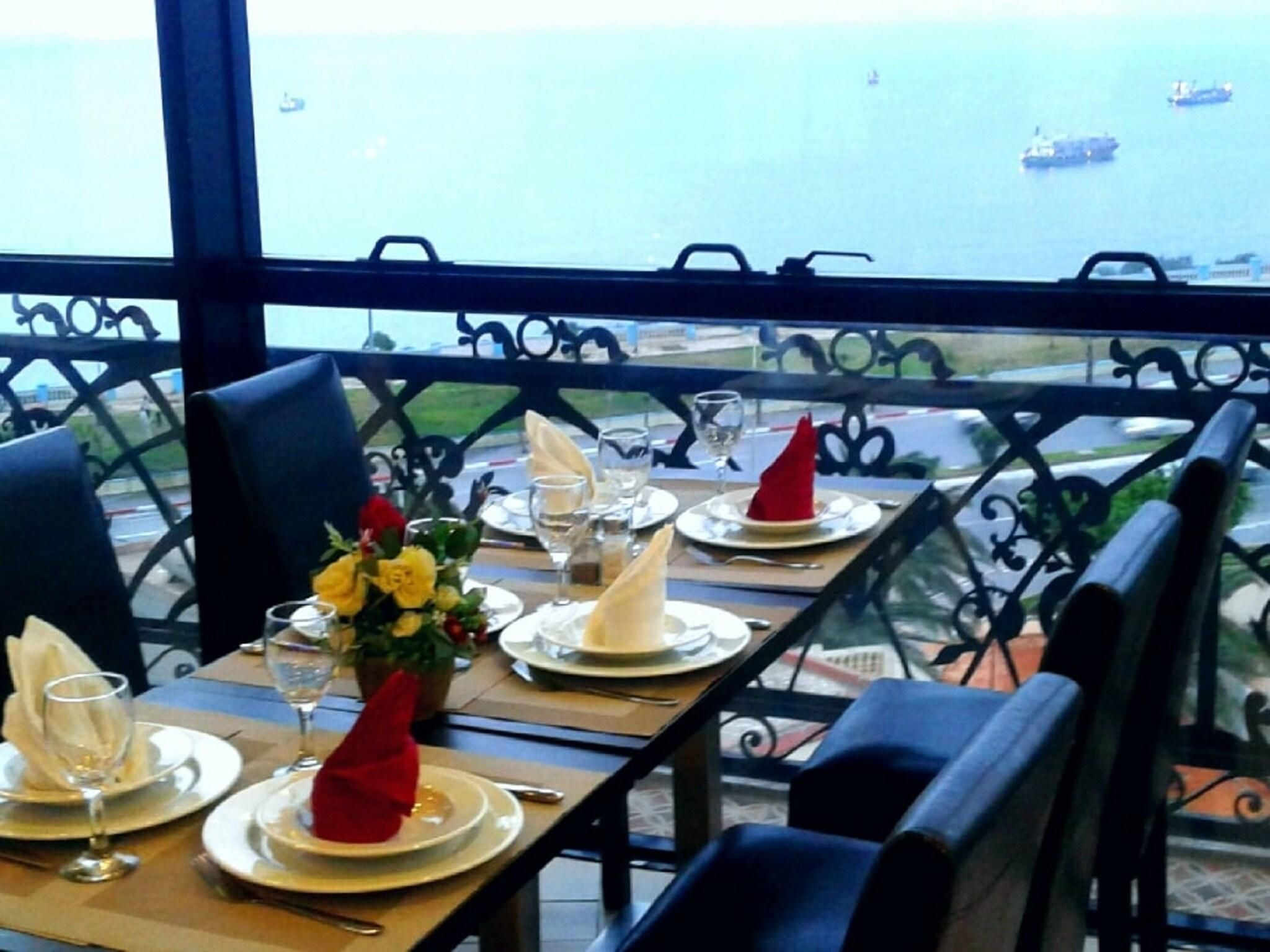 An outdoor dining area with tables set for two, overlooking a body of water with boats.