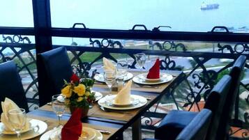 An outdoor dining area with tables set for two, overlooking a body of water with boats.