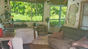 A rustic living room with a sofa, a round rug, and a window with a view of greenery. - The Mud House (Raglan)