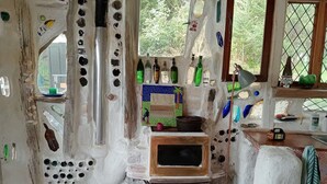 A rustic room with a wooden stove, a television, and various bottles and decorations on the walls. - The Mud House (Raglan)