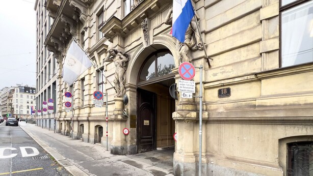 Un edificio histórico con arquitectura clásica, una bandera y varios carteles de prohibido estacionar.