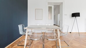 Un comedor moderno con una mesa blanca y sillas transparentes, una lámpara de pie negra y una puerta que da a otra habitación.