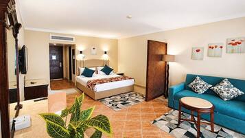 A hotel room with a bed, a sofa, a small round table, and a potted plant.