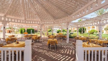 An outdoor dining area with tables and chairs, a pergola structure, and a garden view.