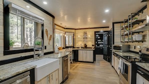 A modern kitchen with a central island, built-in appliances, and a large window providing natural light. - Double home escape in the trees (Angel Fire)
