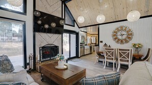 A spacious living area with a fireplace, wooden ceiling, and modern furnishings. - Double home escape in the trees (Angel Fire)
