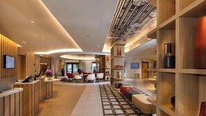 Una hall moderna di un hotel con scrivania della reception, area salotto e soffitto decorato.