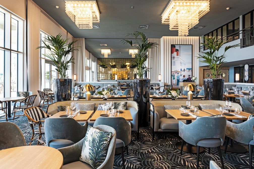 Un restaurante moderno con techos altos, candelabros y una zona de bar central.