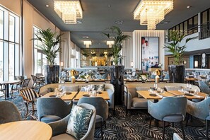 A modern restaurant with high ceilings, chandeliers, and a central bar area. - Thalazur St Jean de Luz (Saint-Jean-de-Luz)