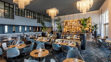 Un restaurante moderno con varias zonas de comedor, techos altos y lámparas contemporáneas.