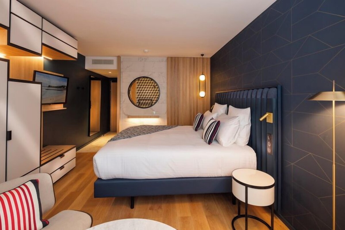 A modern bedroom with a large bed, bedside tables, a TV, and a round wall decoration.