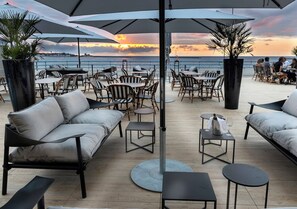 An outdoor seating area with tables and chairs, umbrellas, and potted plants. - Thalazur St Jean de Luz (Saint-Jean-de-Luz)