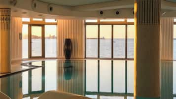 A spacious indoor area with a glass floor, large windows, and a view of the water.