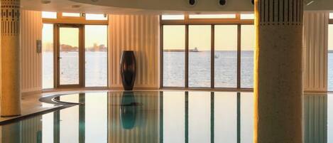 A spacious indoor area with a glass floor, large windows, and a view of the water.