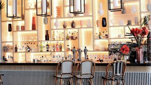 Angolo bar con scaffali pieni di bottiglie, due poltrone in vimini e lampade a sospensione.