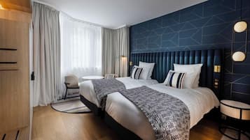 Habitación de hotel con dos camas, una mesa redonda, una silla y un gran ventanal con cortinas.