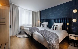A hotel room with two beds, a round table, a chair, and a large window with curtains. - Thalazur St Jean de Luz (Saint-Jean-de-Luz)