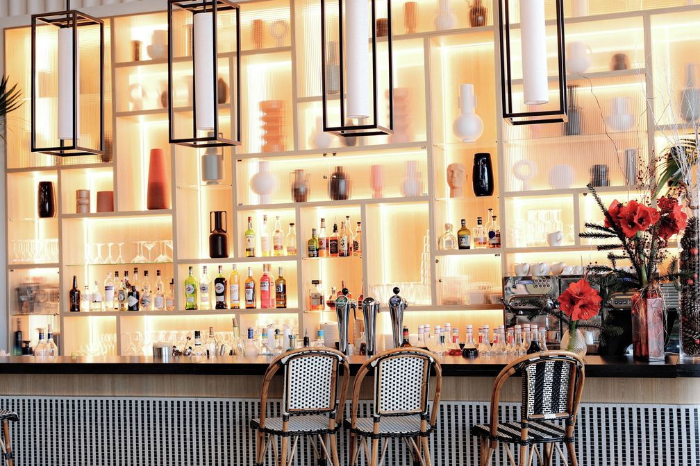 A bar area with shelves of bottles, two wicker chairs, and hanging pendant lights.