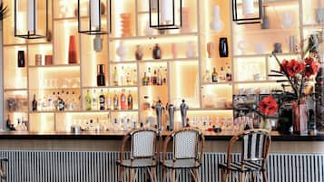 A bar area with shelves of bottles, two wicker chairs, and hanging pendant lights.