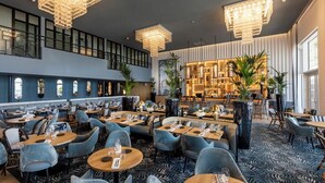 Un ristorante moderno con diverse zone pranzo, soffitti alti e lampade dal design contemporaneo.