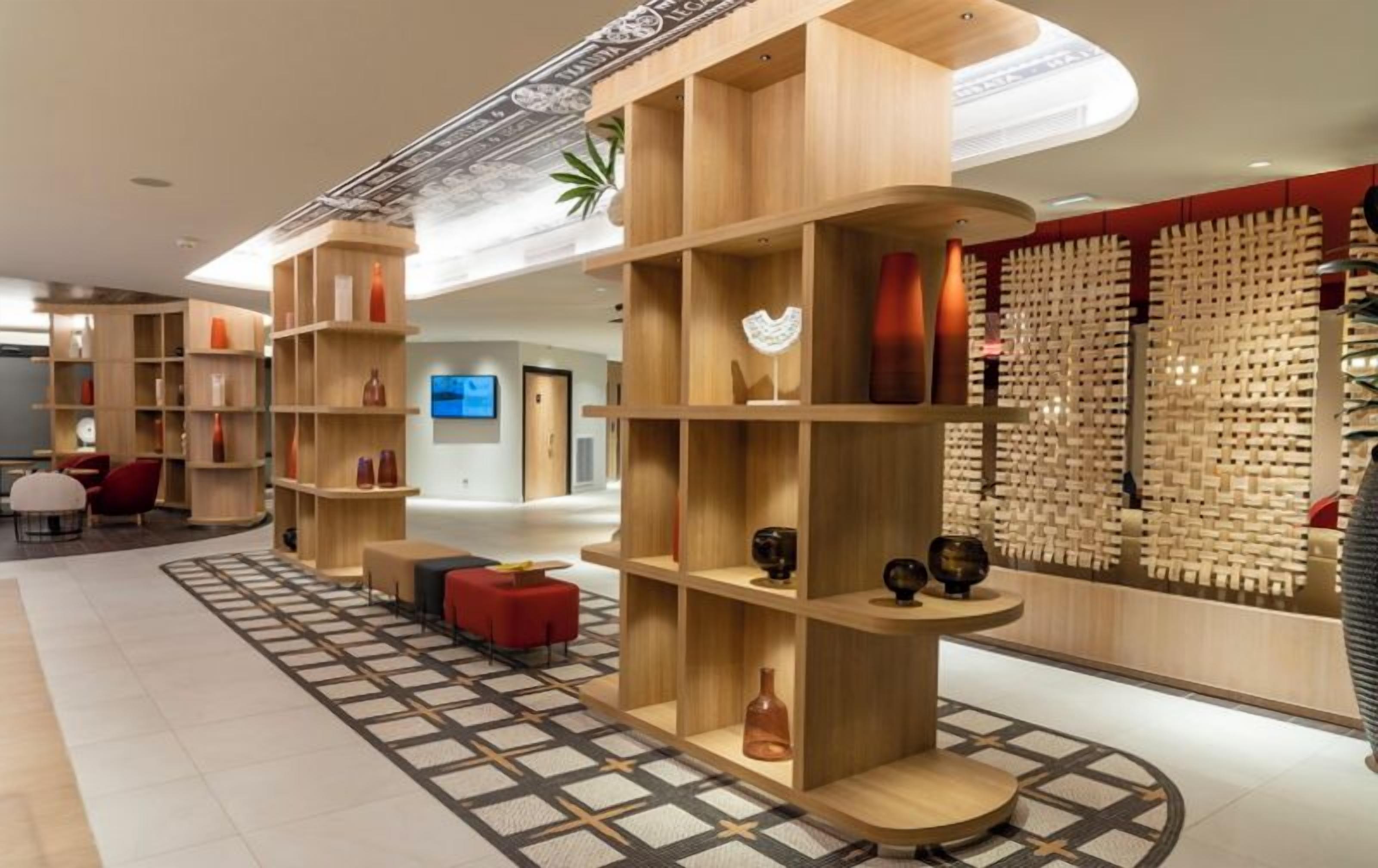 A modern hotel lobby with wooden shelving units, a patterned floor, and a wall of woven textiles.