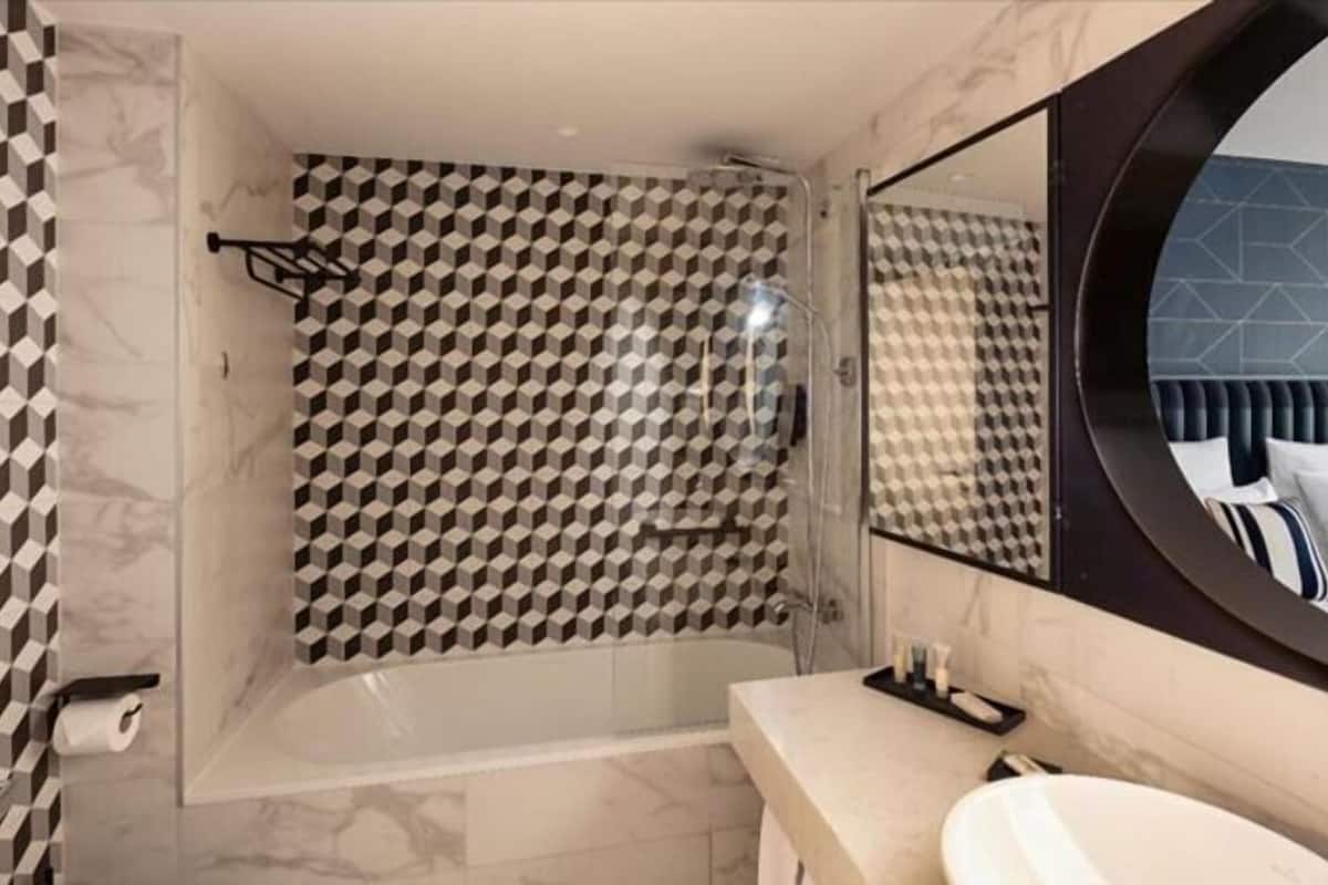 Ein modernes Badezimmer mit einer Dusche im geometrischen Muster, einem runden Spiegel und einem мрамориerten Waschtisch.