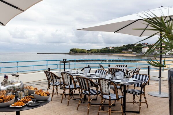 An outdoor dining area with tables and chairs, overlooking a coastal view. - Thalazur St Jean de Luz (Saint-Jean-de-Luz)