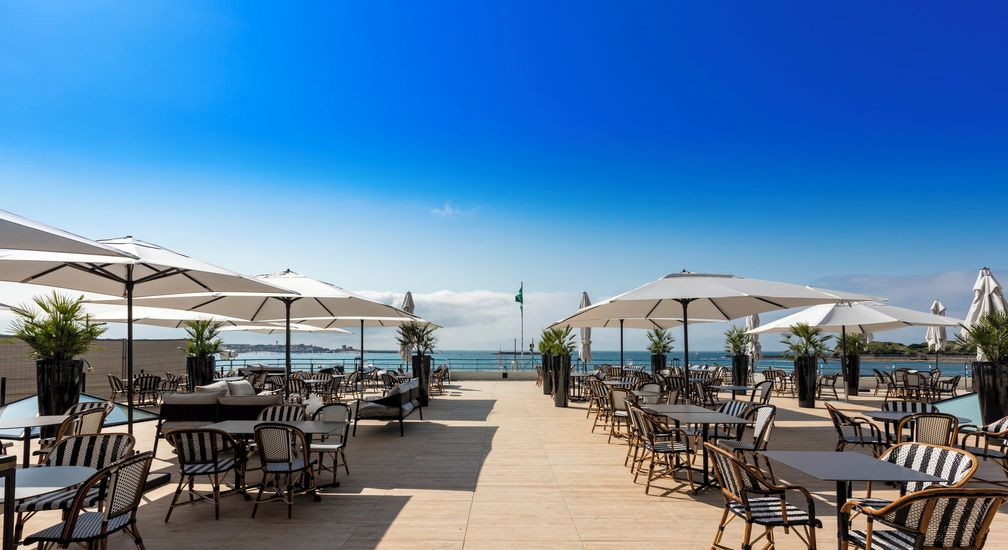 A beachside patio with outdoor seating, umbrellas, and a view of the ocean.