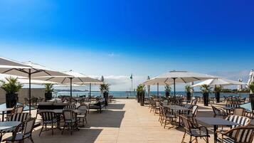 A beachside patio with outdoor seating, umbrellas, and a view of the ocean.