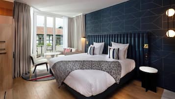 Una habitación de hotel moderna con una cama grande, un área de descanso con una silla y una mesa, y vistas al exterior a través de la ventana.