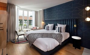 A modern hotel room with a large bed, a seating area with a chair and table, and a view of the outdoors through the window. - Thalazur St Jean de Luz (Saint-Jean-de-Luz)