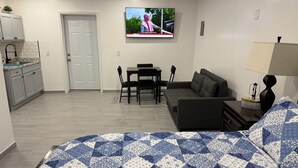 Een knus woongedeelte met een bed, een slaapbank, een eettafel met stoelen, een keuken en een aan de muur bevestigde televisie.