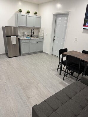 A modern kitchen with grey cabinets, a stainless steel refrigerator, a marble countertop, and a dining area with a dark wooden table and black chairs. - Wonderful 1-bedroom apartment with AC in vibrant Orlando (Orlando)