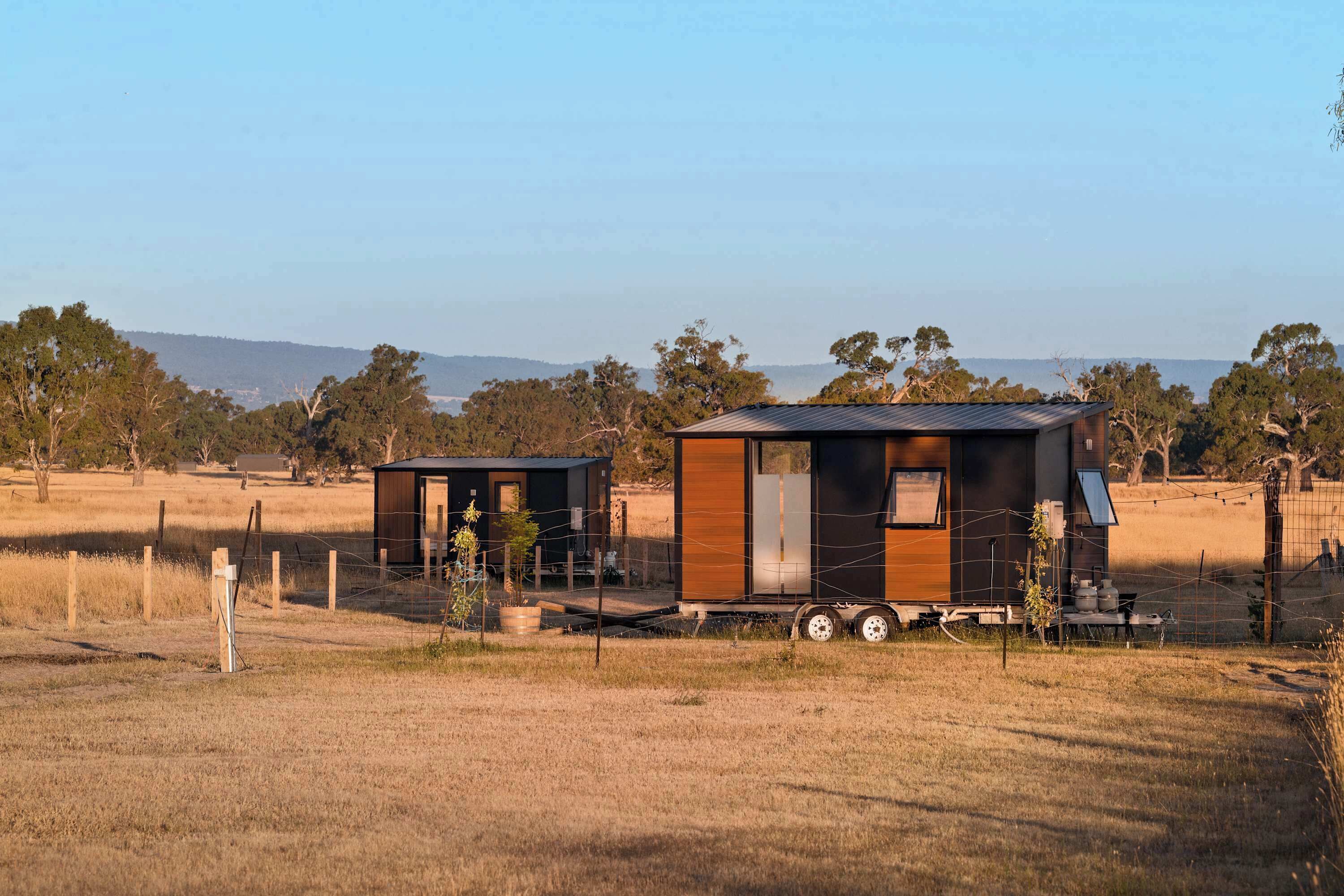 Deux petites cabanes modernes, situées dans un cadre rural, offrent une vue dégagée sur le paysage environnant.