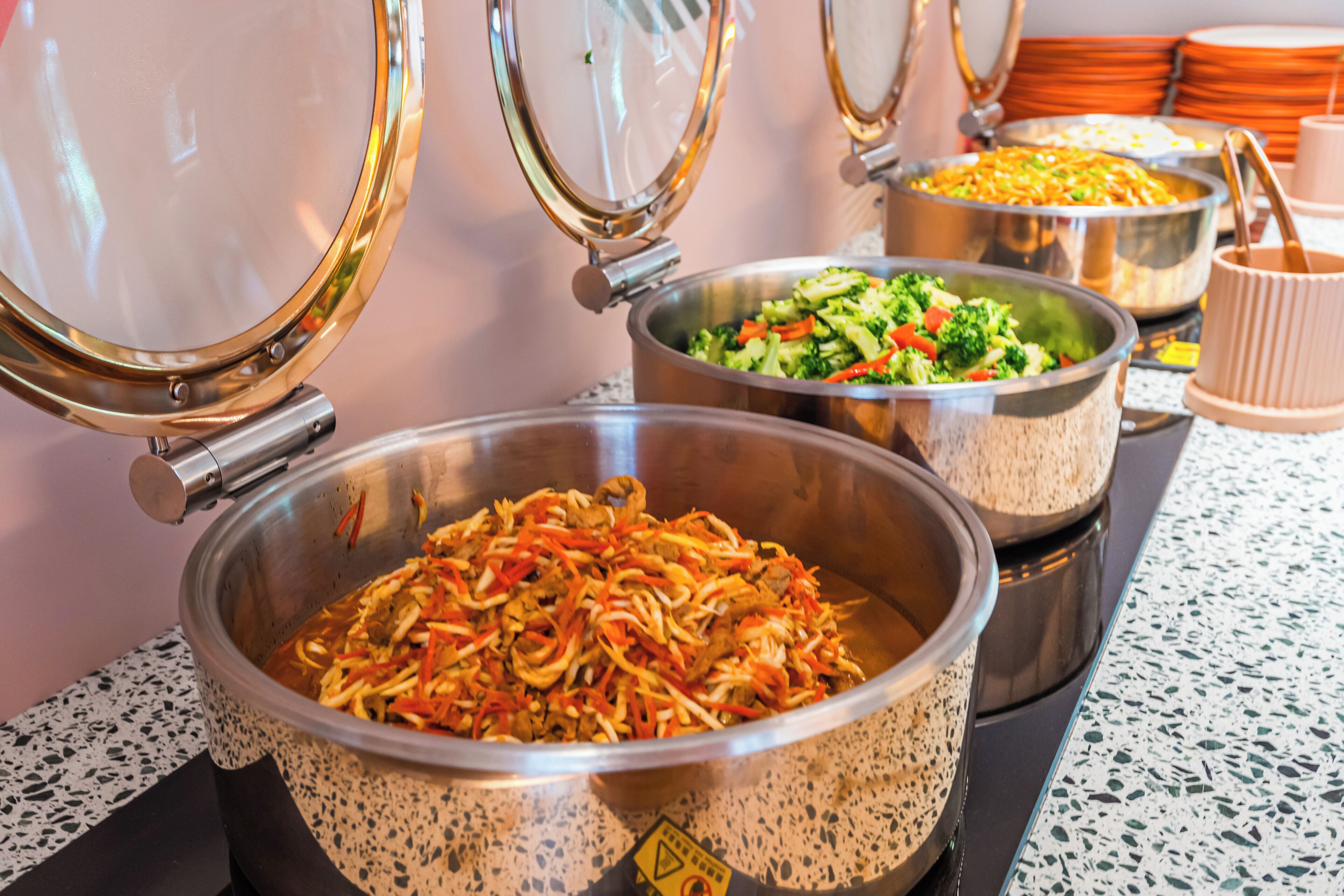 A buffet with various dishes, including a large bowl of noodles, a salad, and other food items.