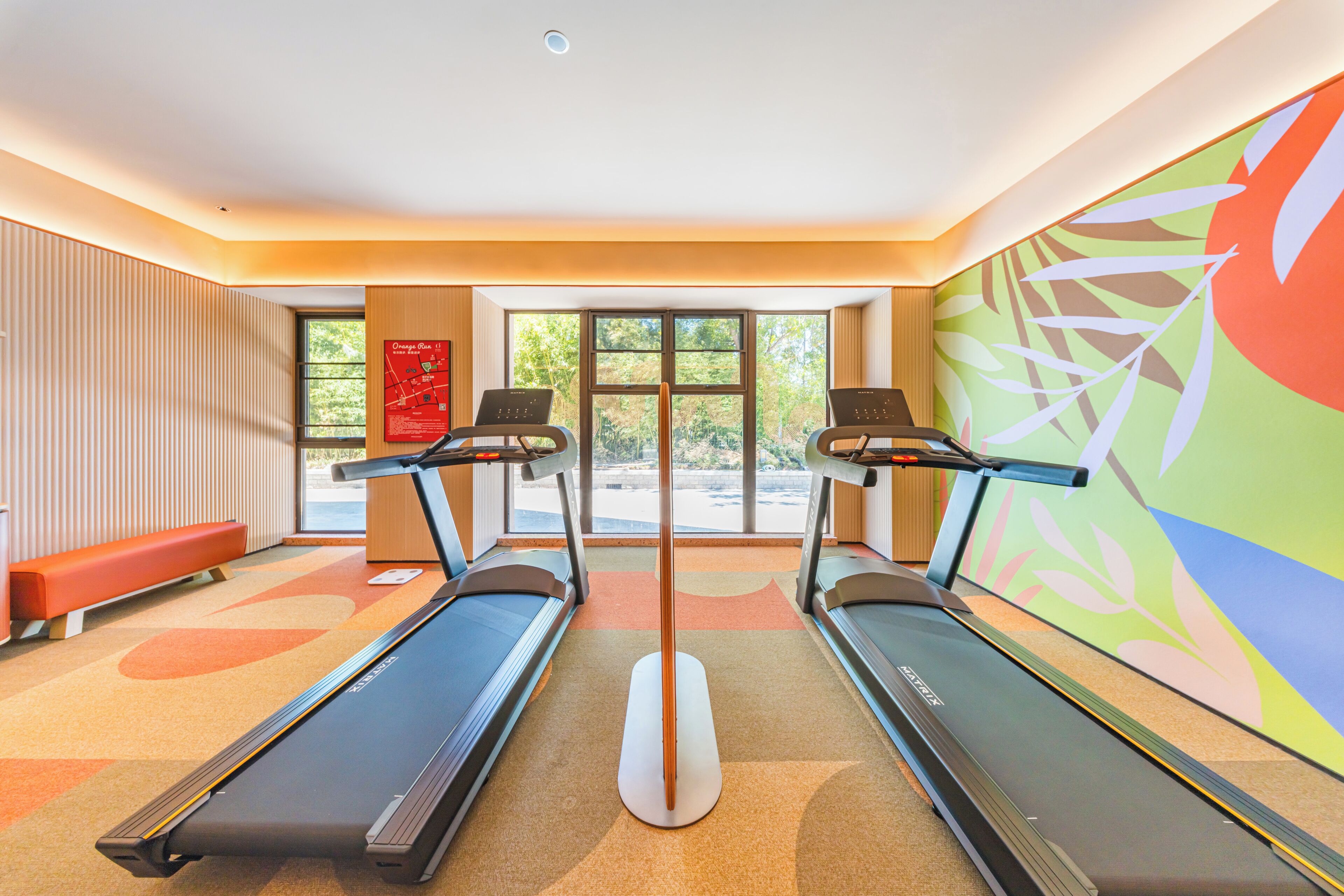 A gym with two treadmills, a bench, and a large window with a view of trees.
