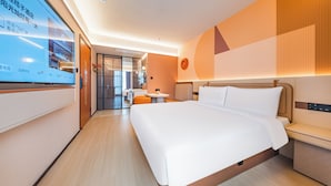 A modern hotel room with a large bed, bedside tables, a small round table, and a TV screen displaying hotel information. - Orange Hotel (Shanghai)