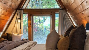 Un dormitori acollidor amb un llit gran, vàries almoines i vista a un bosc a través d'una porta de vidre.