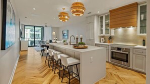 Une cuisine moderne dotée d’un îlot central, de tabourets de bar, de luminaires suspendus et offrant une vue sur l’espace de vie.