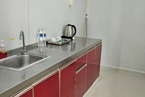 A modern kitchen with stainless steel countertops, a sink, and red cabinetry. - Saga Village Hotel & Resort Bintan By Zuzu (Bintan)