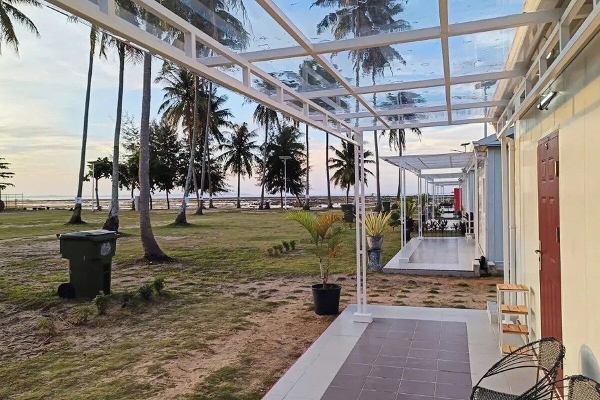 A covered outdoor area with a view of the beach, palm trees, and a building with a red door.