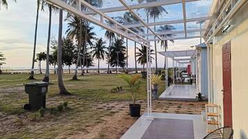 A covered outdoor area with a view of the beach, palm trees, and a building with a red door.